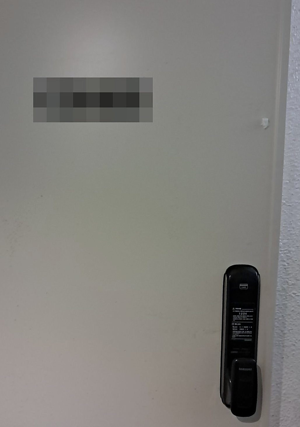만안구 병목안동 출장 — 밝은 회색 문 오른쪽 아래에 달린 검은 푸시풀 도어락과 카드 표시, 안내 스티커