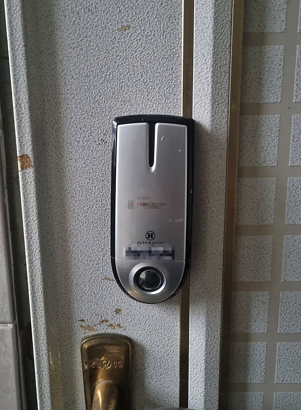 만안구 호현동 출장 — 오톨도톨한 회색 철문에 달린 은색·검정 번호키와 아래 청동빛 손잡이 윗부분